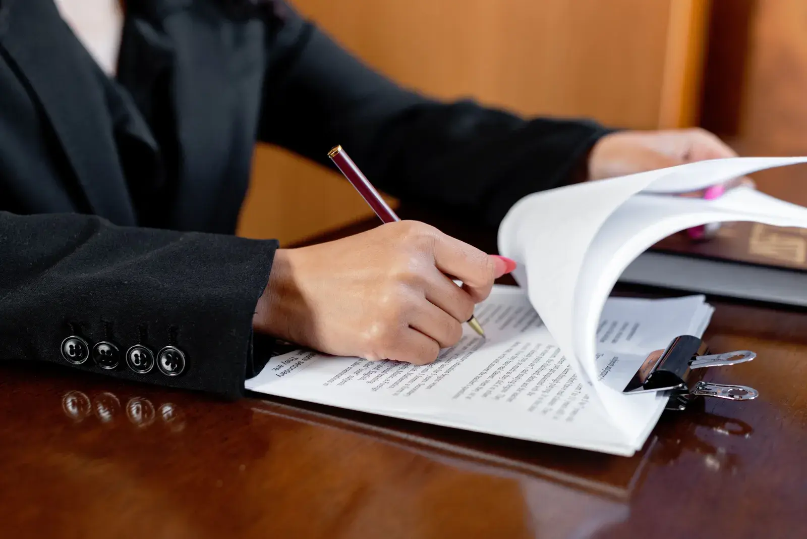 A person in a dark suit annotating a printed report with a pen at a wooden desk
